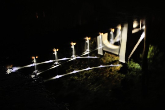 Rozmazane odbicie mostu nocą w tafli wody.