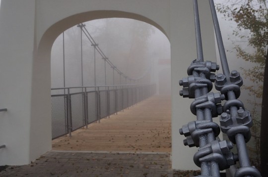 Widok na most, w tle mgła. Na pierwszy planie łańcuch trzymający most wiszący.
