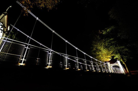 Most wiszący nocą, oświetlony iluminacją.