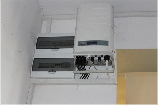 Urządzenie w metalowej skrzynce służące do obsługi paneli fotowoltaicznych, służące do regulacji temperatury. Białe ściany.