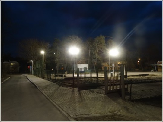 Widok na oświetloną lampami ledowymi drogę oraz na boisko do gry w koszykówkę.