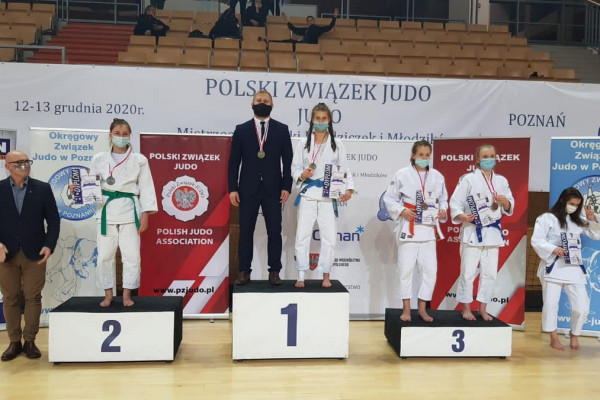 Sala widowiskowa. Na pierwszym planie podium, na którym stoją zawodnicy i ich trenerzy. w tle trybuny i kibice.